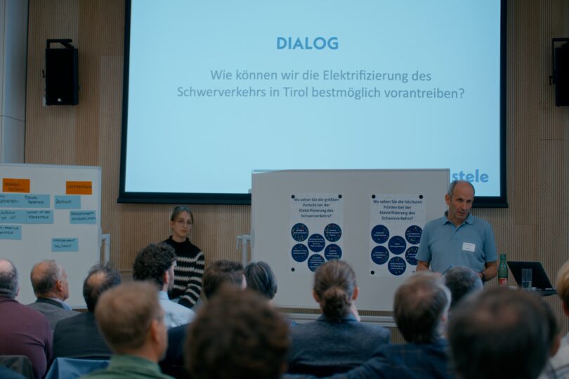 Die Dialogrunde wird vor einem Moderator, der vor dem Publikum steht, moderiert.